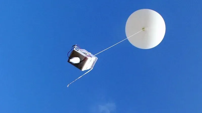 A radiosonde instrument package carried aloft by a weather balloon against a clear blue sky