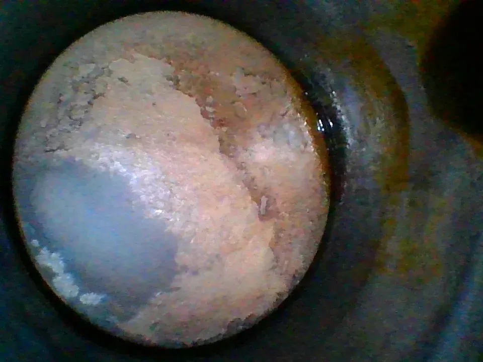 Borescope view of a dark, wet, oily piston crown showing oil working past the rings