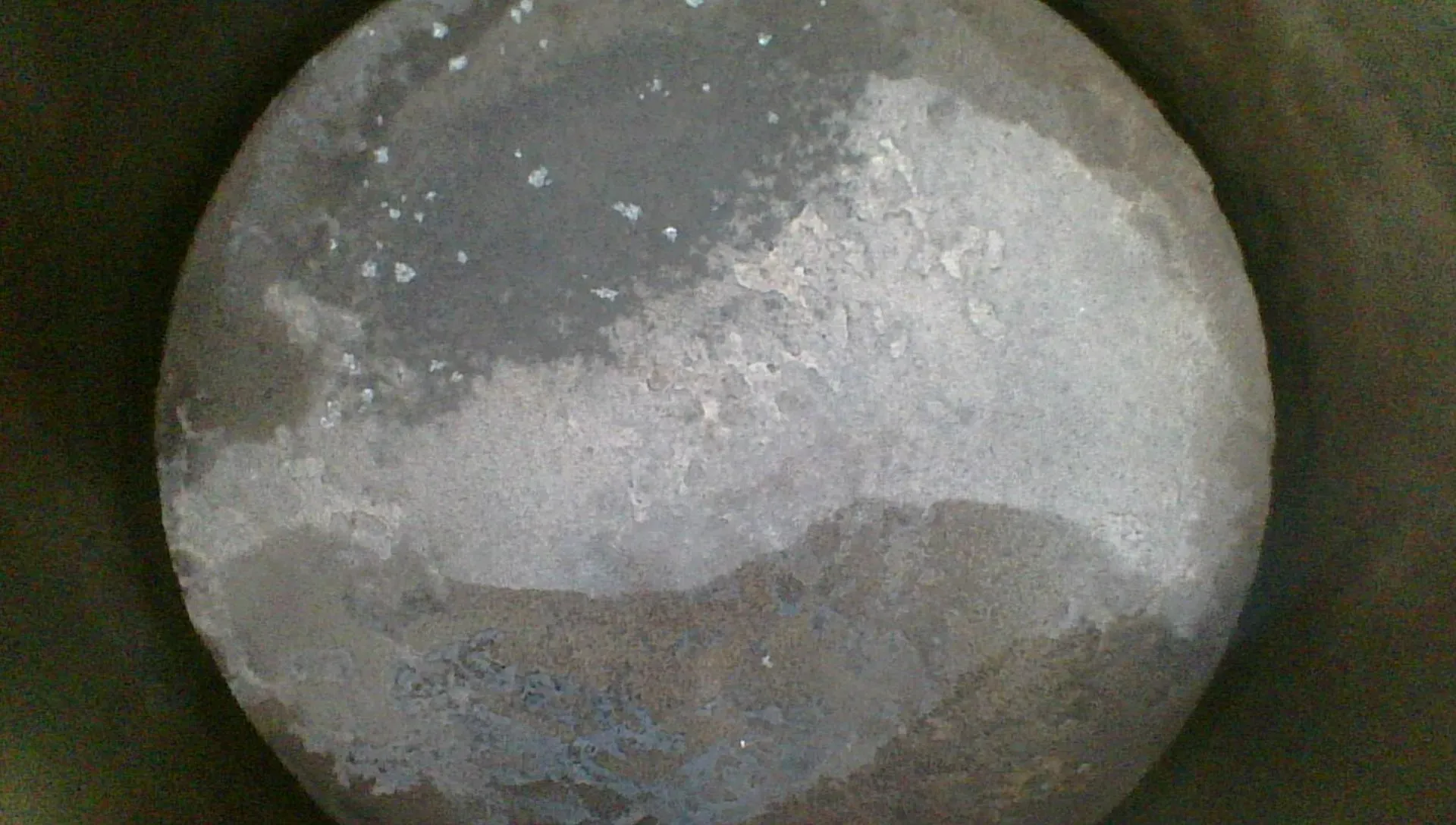 Borescope view straight down onto a piston crown showing even gray-tan combustion deposits