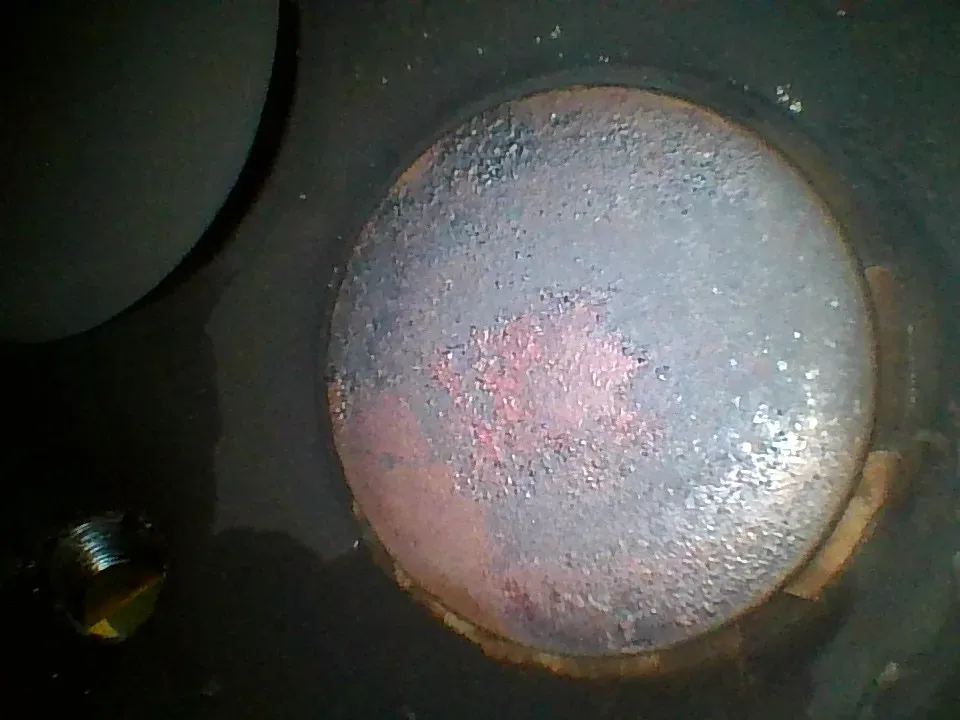 Borescope view of a distressed exhaust valve face with a pink washed-out hot spot and loss of the even concentric pattern